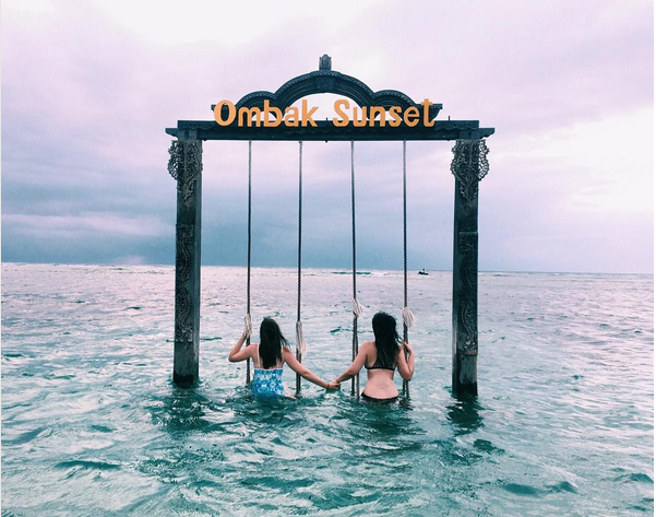 Two young women sit on a double swing in the ocean of Gili Trawangan