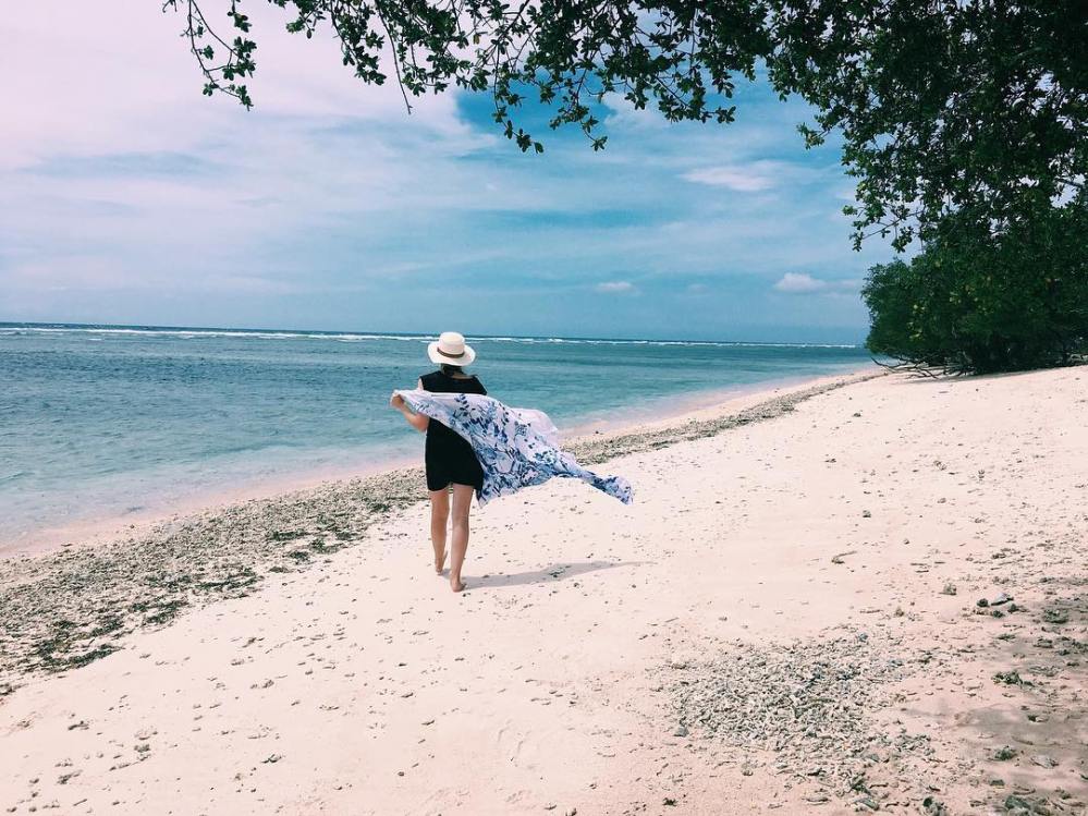 Woman strolls along the beach of Gili Trawangan with her sarong blowing in the wind