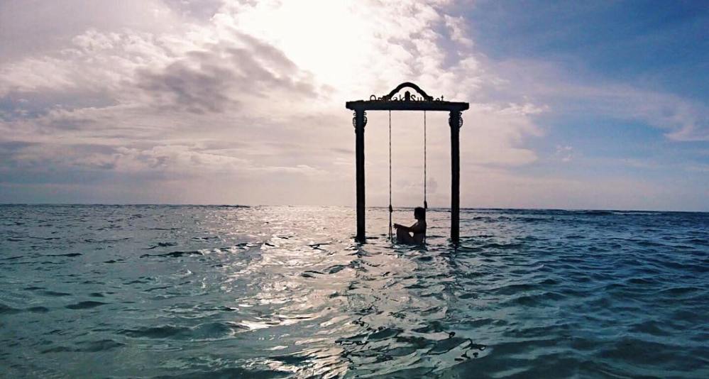 Woman sits on a swing in the ocean on Gili Trawangan