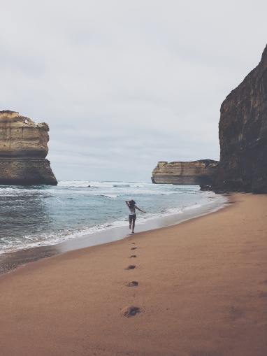 Girl running along the beach, surrounded by cliffs at the Twelve Apostles in Victoria, Australia