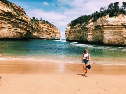 Woman walking along the beach, surrounded by limestone formations at the Loch Ard Gorge in Victoria, Australia