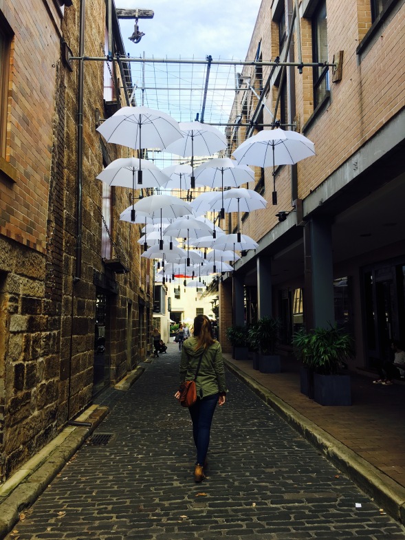 Woman walks on a cobblestone path below an art installation of umbrellas